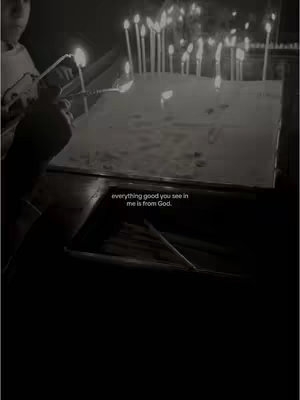 The image is a black and white photo of a religious scene. Several candles are lit, the flames visible as bright points of light. In the foreground, a person's arm and hand appears to be involved in lighting a candle as well. The text overlay states, "everything good you see in me is from God."