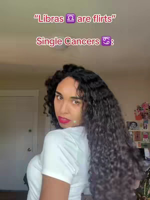 A woman with long, dark, curly hair is seen from the chest up, turned slightly to the left. She's wearing a white top and has bright red lipstick. Text overlays are at the top of the screen.