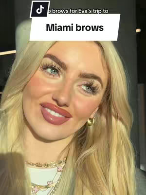 A close-up shot of a woman with blonde hair posing with vibrant makeup. She has long eyelashes, glossy pink lips, and gold hoop earrings. The background is blurred, focusing attention on her face. Text overlays are present.