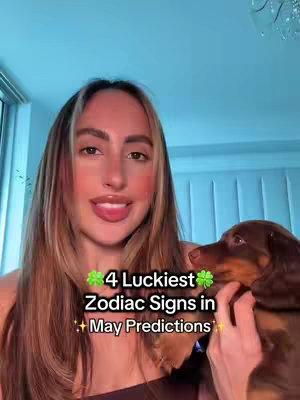 A woman with long, light brown and blonde hair is smiling at the camera while holding a small brown and black dog in her arms. Text overlays the photo with a title about lucky zodiac signs.