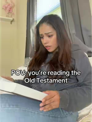 A young woman sits on a bed reading a large book, likely a Bible, near a window with curtains. Text overlay on the image reads "POV: you're reading the Old Testament."