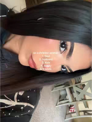 Close-up shot of a woman's face, angled slightly to the side. She has long, dark hair and is wearing makeup. Text overlays list "as a christian woman" followed by a numbered list: "1. God", "2. husband", "3. kids", "4. family", and "5. friends."