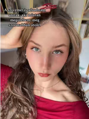 A close-up selfie of a person with long wavy hair, looking directly at the camera. Text is overlaid at the top. The person wears a red shirt and has visible light makeup, with a necklace. The background is slightly blurred.