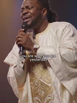 A man in a white and gold embroidered outfit is singing into a microphone. Text overlays the image.