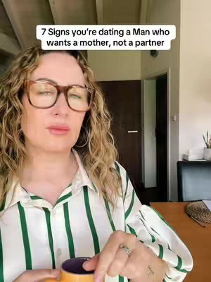 A woman with curly blonde hair and glasses is holding a mug with both hands, while looking at the camera. A text overlay reads "7 Signs you're dating a Man who wants a mother, not a partner". The background is slightly blurred, showing interior elements.