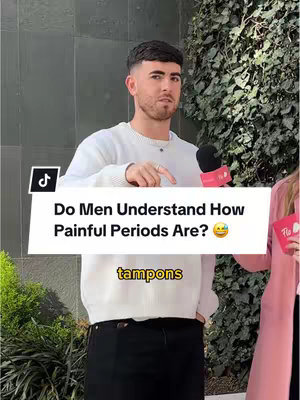 A man stands pointing a finger, dressed in a white sweater and black pants, with a microphone nearby, the video's text overlay asking, 'Do Men Understand How Painful Periods Are?' with a smiley emoji. The background suggests an outdoor setting with greenery and building structures.
