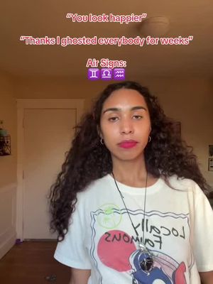 A selfie-style video cover image featuring a woman with long, dark curly hair and wearing a white t-shirt. Text overlays include quotes and discussion about zodiac signs. The background is a warm-toned interior.