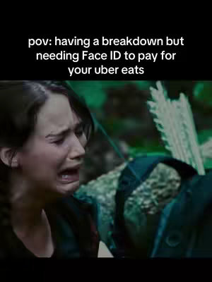 The cover image shows a still from a movie featuring Jennifer Lawrence as Katniss Everdeen, with a close-up of her tearful face. The background is blurred, showing foliage and parts of what appears to be a costume, framing the emotional expression of the character. Text overlays at the top describe the scenario.