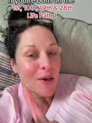 A woman with dark curly hair frames the shot, facing toward the camera with a thoughtful expression. The text overlay suggests a numerology concept. The background includes a portion of a striped pillow behind a neutral couch, and the subject wears a light pink top.