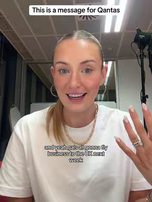 The video shows a woman in a close-up shot. She is smiling at the camera, with text overlays above and below her. She is wearing a white t-shirt, a gold necklace, and hoop earrings. Her hair is pulled back in a ponytail.