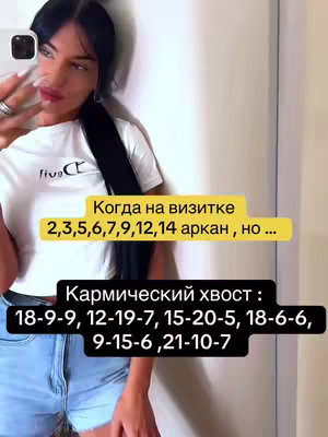 A woman in a white shirt and denim shorts holds her phone up to take a selfie in a well-lit room. Text overlays on the screen indicate content related to tarot and karmic destiny.