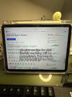A tablet displaying a UCAT mock test interface is prominently featured. Text overlays the screen, offering advice for the exam questions. The setup also consists of a keyboard and desk surface.