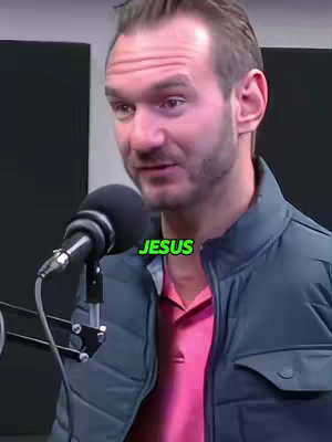 A medium shot features a man speaking into a microphone, with the word "JESUS" in a green box overlaid on the image. The man has short hair and is wearing a blue jacket over a pink shirt, set in a studio environment.