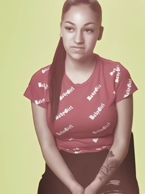 The cover image features a woman with dark hair pulled back into a low ponytail positioned with a slightly downward angle. She has a neutral expression, looking slightly off-center. She's wearing a red t-shirt with a repeating white 'Baby Girl' text design. The background is a solid, light green color and the lighting seems even, with no strong shadows. The woman is sitting. She has a tattoo on her right arm.