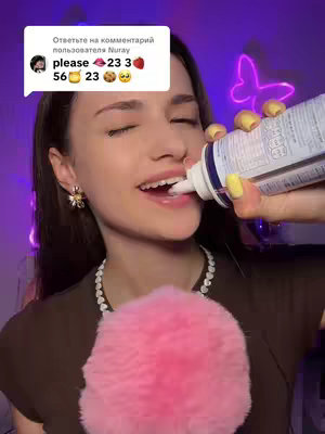 A woman holds a can of whipped cream to her mouth. The can is white and blue. She is wearing a brown top and a beaded necklace and a sparkly earring. Her left hand is covered with a pink fluffy poof. The top left corner has a white bubble with text, along with emojis above a set of numbers.