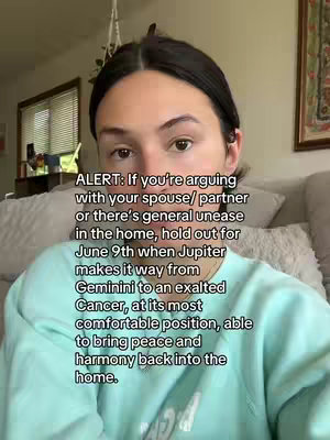 A woman with dark hair is centered in the frame, looking towards the viewer. She has a neutral expression. The background is a soft, blurred setting that suggests a home interior with a window on the left side.