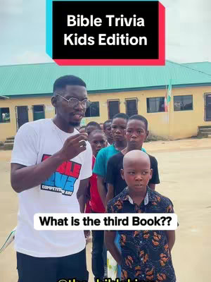 A man in a white t-shirt stands centered in front of a school building, with one student in front and others lined up behind. An overlay at the top reads 'Bible Trivia Kids Edition' in a colorful design. The bottom overlay asks, 'What is the third Book??'
