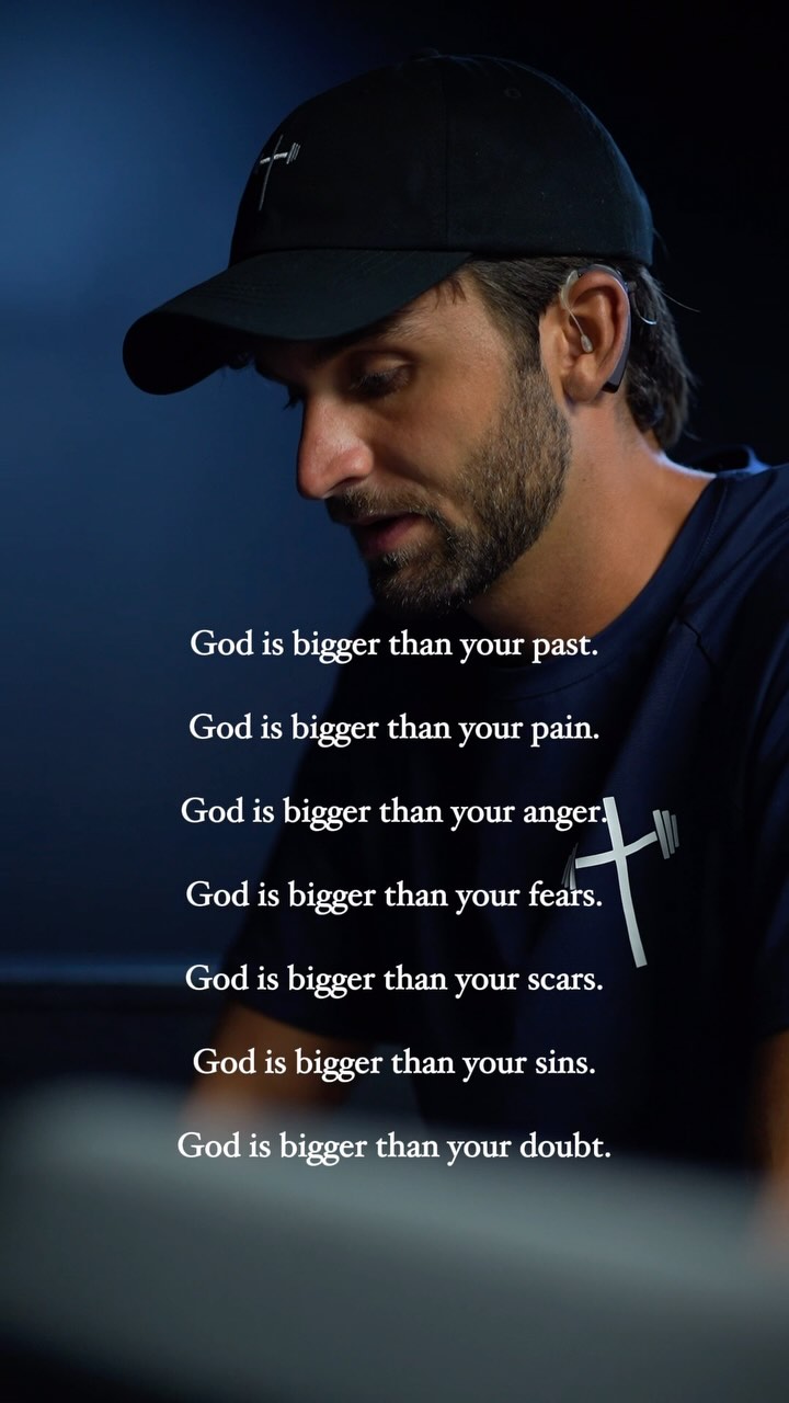 A medium shot shows a man against a dark blue background. He wears a black baseball cap with a white cross-and-barbell logo, and a dark blue shirt. White text is layered over the image, and quotes a motivational spiritual message.