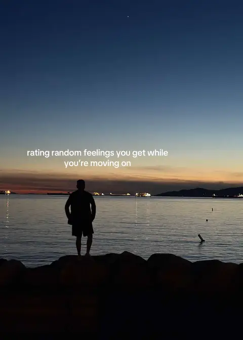 A silhouette of a person standing on a rocky outcrop, facing away from the camera towards a tranquil seascape. The sky transitions from deep blue at the top to a warm orange and yellow near the horizon, suggesting a sunset. Distant boats and a suggestion of land can be seen on the water. Text overlay reads 'rating random feelings you get while you're moving on.'