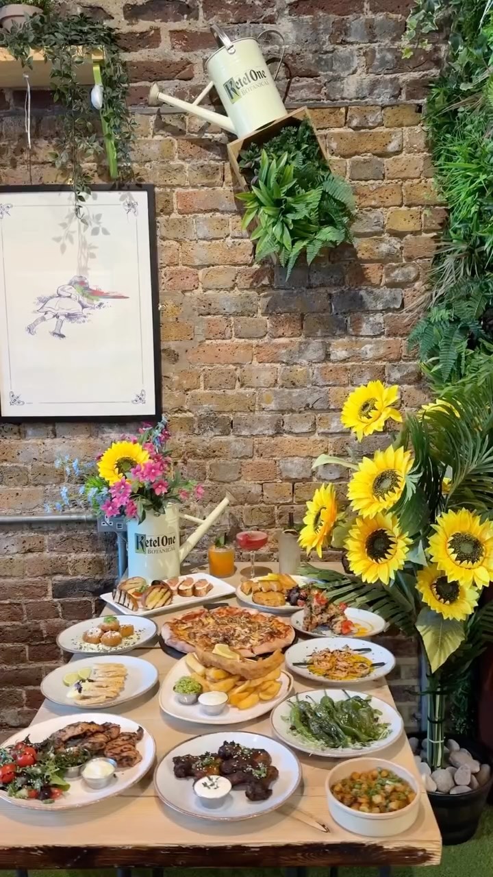 The cover image displays a table laden with food items in front of a brick wall with sunflowers and plants. The table includes various plates of food, a pizza, sides, and glasses with drinks.
