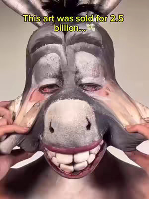 A close-up shot of a person's face, altered to resemble a donkey's head, is shown. The person's skin is painted gray and white to mimic the donkey's fur, with the person's real eyes still visible above the donkey 'face' makeup. The person is pulling their skin to the side of their face, revealing teeth and smiling. Above the face, text reads, 'This art was sold for 2.5 billion...' in yellow text.