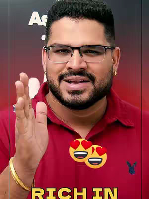 A man with glasses smiles at the camera, with his hand raised in a gesture. Heart-eyed emojis are added to the image.