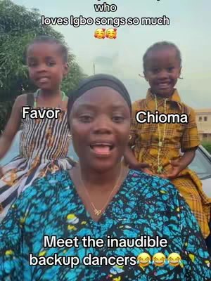 A woman with a dark head covering stands in the center, smiling and appearing to sing or speak. Two young girls are positioned on either side of her, with the one on the left wearing a patterned dress, and the one on the right in a yellow and black patterned top. Text overlays are visible, identifying the girls as 'Favor' and 'Chioma.'