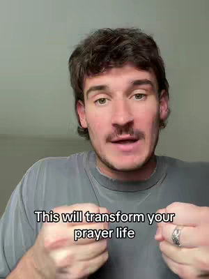 A man with dark hair and a mustache is centered in the frame, wearing a gray t-shirt. Text overlayed below reads 'This will transform your prayer life'. He is looking directly at the camera and has a calm expression, with his hands clenched. The background is a plain, neutral color.