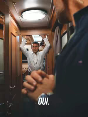 The cover image shows a man in a white shirt reflected in a mirror. The man is holding his arms up, leaning against the doorway of what appears to be a train cabin. Another man is at the right, out of focus with a dark jacket. At the bottom, the word 'OUI' can be seen. The color palette is warm, with a focus on wood tones and highlights of light.