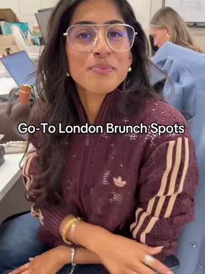 A woman with dark hair and glasses smiles at the camera while seated. The background includes a desk and another person partially visible. The video title is overlaid at the bottom.