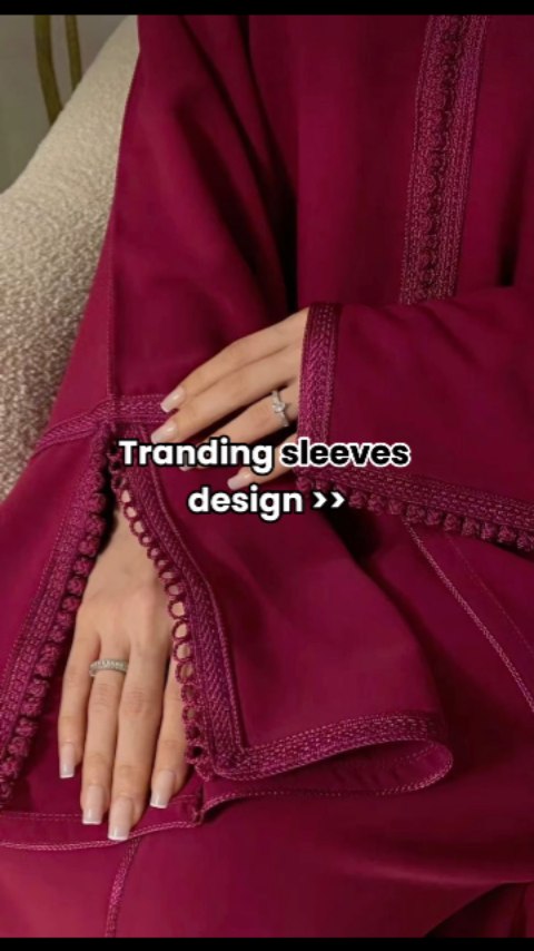 The image features a close-up of a person's hands and arms. The main focus is on elegant burgundy sleeves, revealing manicured nails and a ring. The text overlay states "Trending sleeves design >>", suggesting a fashion-related video. The composition is simple, highlighting the texture and detail of the sleeves, likely showcasing design trends.