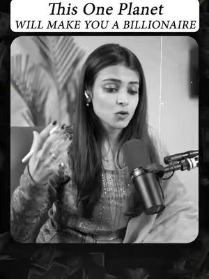 A black and white image of a woman with long hair and a microphone, speaking intently, with a text overlay above. She is wearing a patterned top and earrings, and is inside a room with a light background with other objects in the back that create a kind of interview vibe setup.