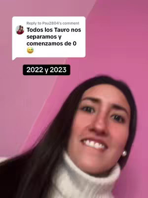 A woman with dark hair and a white turtleneck is captured in a selfie-style shot. A pink background fills most of the frame. A comment bubble at the top left contains white text on a dark background. Below this is black text reading, "2022 y 2023".