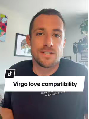 A man with short brown hair is looking at the camera. He is wearing a black t-shirt. Above him is a white banner with the text 'Virgo love compatibility' and below that is a smaller text that says 'these kind...don't really matter'. The background includes artwork of what seems to be abstract art, with a wooden framed circular floral pattern, and other miscellaneous items, one of them is a black bag.