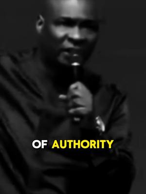 A grayscale image features a dark-skinned man with a shaved head, holding a microphone near his mouth. He is dressed in a dark-colored, long-sleeved shirt. Text overlayed on the lower portion reads 'OF AUTHORITY', highlighted in a yellow font.