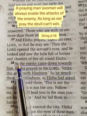 The image is a close-up shot of a Bible page with highlighted text. The text overlayed in a yellow rectangular box reads 'A praying man \woman will always evade the attacks of the enemy. As long as we pray the devil can't win.' There's a blue pen pointing to a specific line, and the page is lightly aged with visible print. The lighting is natural.