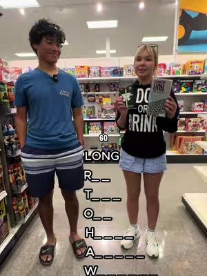 Two people, a man and a woman, stand inside a retail store. The man is on the left, and the woman is on the right, holding two books. Large white text overlays the image. The background shows store shelves filled with various products.