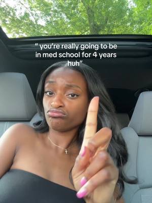 A selfie showing a woman inside a car. The woman is looking toward the camera with a slightly sour expression, and she's pointing one finger up. In the background, you can see a view of the trees through the sun roof of the car.