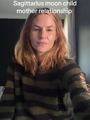 A woman with light brown hair, wearing a dark green and black striped top. The background seems to be a room with curtain.