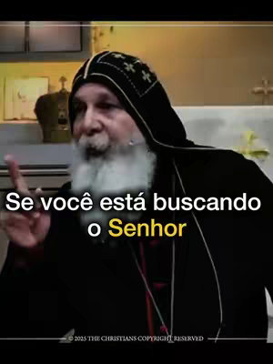 The image shows an older man wearing a dark high-collared garment with a black hood, pointing his finger at the viewer.