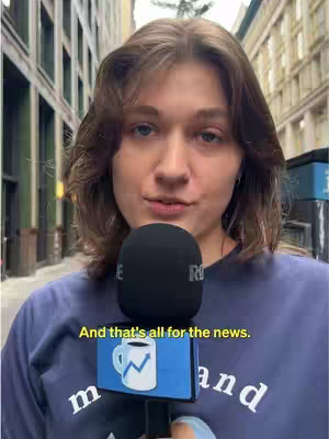 Woman in a blue shirt holding a microphone with a logo, standing in a street with buildings on either side. The background is blurred. There is a text overlay at the bottom.