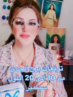 The cover image is a selfie-style video featuring a woman in a room with several objects in the background, and the video has text at the bottom. She is wearing glasses and has her hair pulled back. Behind her are some small colorful circle decorations and a poster. At the upper left can be seen a stack of tarot cards. There are multiple spiritual themed items on the table and behind including candles and a small golden-colored Youtube awards looking item. The text at the bottom describes dates in Arabic.