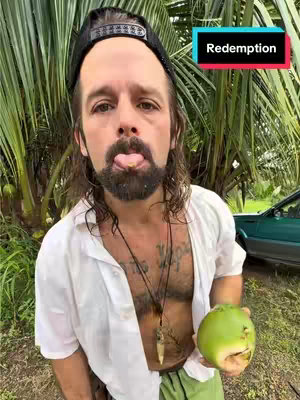 A man with a beard, wearing a black hat is sticking his tongue out and holding a green fruit. The word 'Redemption' is displayed on a colored rectangle in the top right, while large plants and a vehicle fill the background with a well-lit outdoor scene.