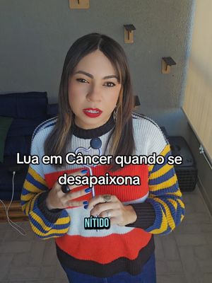 A woman with long, lightly highlighted hair, wearing a sweater with a black, white, red, and yellow pattern. She is looking at the camera with red lipstick. Text appears on the screen in white and a smaller text in a box that says "nítido". The background features a neutral color with some fixtures on the wall.