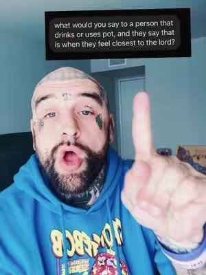 A man with tattoos on his face and head is looking at the camera as he is making the "up yours" gesture or "middle finer" with his right hand. A text overlay on the top shows a question regarding religion and use of drugs. He's wearing a blue hoodie, and the background is slightly blurred.
