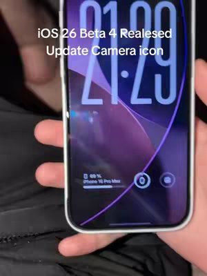A person holds a smartphone displaying a lock screen with a purple and blue background. The lock screen shows the time, with a camera icon, and a battery percentage. Overlay text announces iOS 26 Beta 4 Release, the camera icon update.