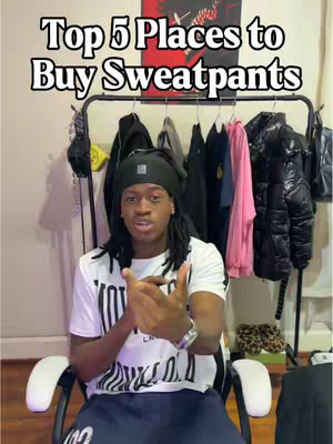 A medium shot featuring a Black male wearing a cap, white shirt with black design, and dark blue sweatpants is seated and speaking to the camera. The text overlay identifies the video topic. Behind him, a rack displays clothing items, indicating a room setting.