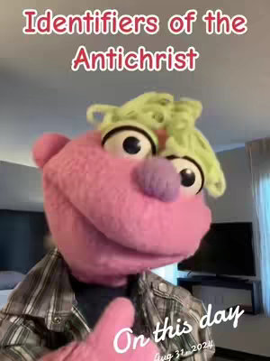 A close-up shot of a puppet with a pink face, green hair, and large eyes. Text overlays the image.
