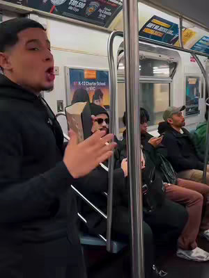 A man in a black hoodie is standing on a subway train, holding a Bible and appearing to preach. He is the clear focus. Other passengers sit in the seats behind and to the side of him. The image has a documentary-style candid feel. The background shows advertising and structural elements of the subway car.
