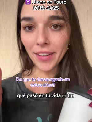 A selfie-style video cover featuring a light-skinned woman with long, dark hair. She is smiling at the camera while partially holding a white travel mug. Text overlays in the upper left reads "Urano en Tauro 2018-2025". Below the woman's face is a text overlay in a purple box, asking a question in Spanish. The overall composition centers on the woman's face with a casual background, and the lighting is bright.